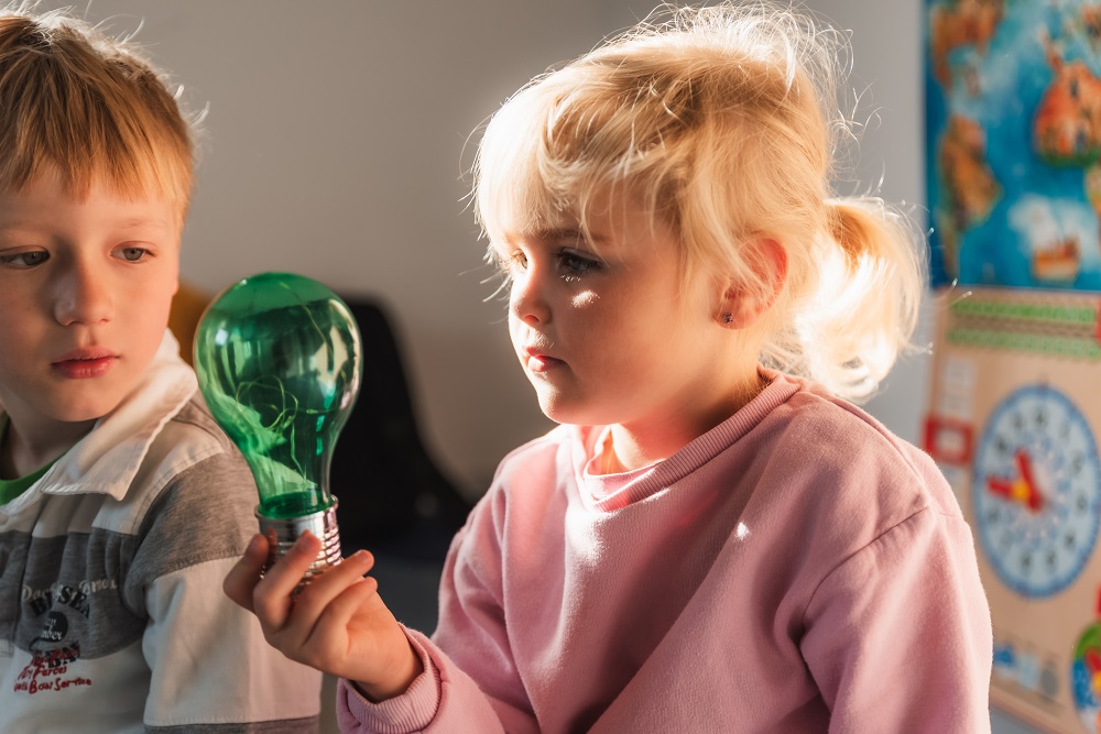 Zwei Kinder betrachten interessiert eine grüne Glühbirne.