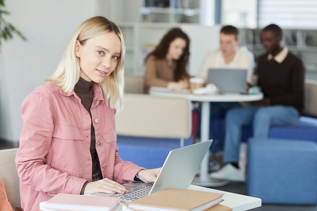 Lächelnde junge Frau mit Laptop in der Bibliothek.