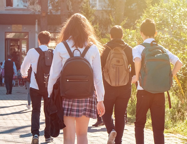 Schülerinnen und Schüler laufen mit ihren Rücksäcken auf ein Gebäude zu.