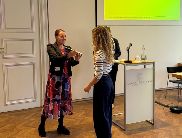 Julia Müller überreicht einer Frau während der Veranstaltung feierlich eine Unterlage
