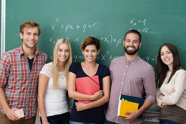 Gruppe von fünf lächelnden Studierenden, die nebeneinander vor einer grünen Kreidetafel stehen.